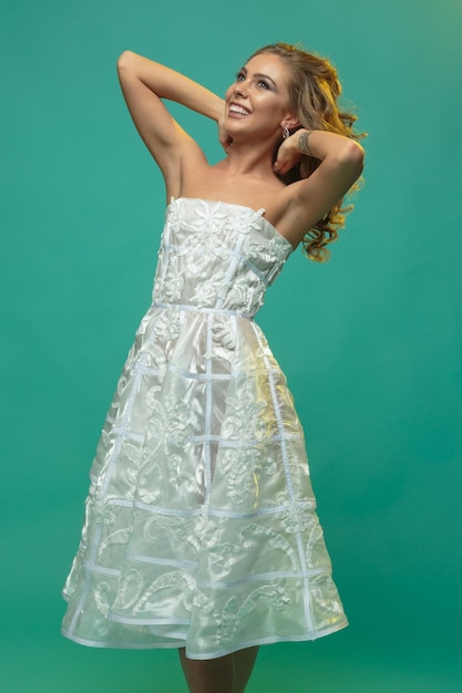 Un portrait vertical d'un jeune mannequin tenant ses mains sur son cou et riant sur fond bleu Photo de haute qualité