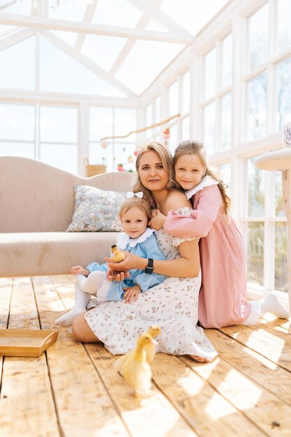 Photo portrait vertical d'une jeune mère heureuse et de deux filles joyeuses en robe jouant avec un petit jaune