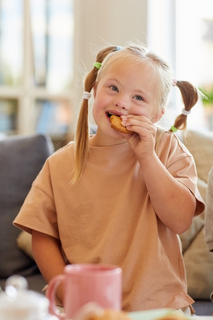 Portrait vertical de jolie fille atteinte du syndrome de Down, manger des biscuits tout en profitant du thé en famille à la maison