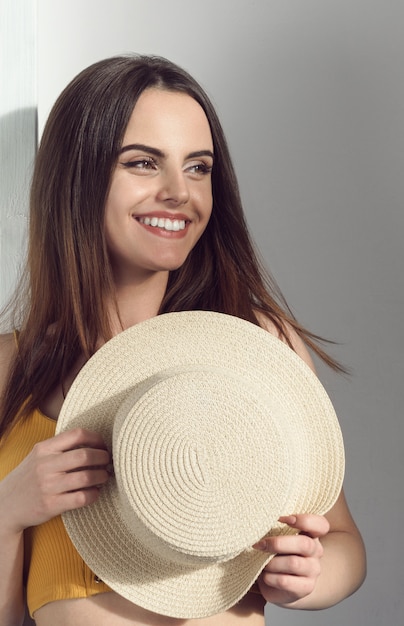 Portrait vertical de jolie jeune fille prenant son chapeau de paille et souriant