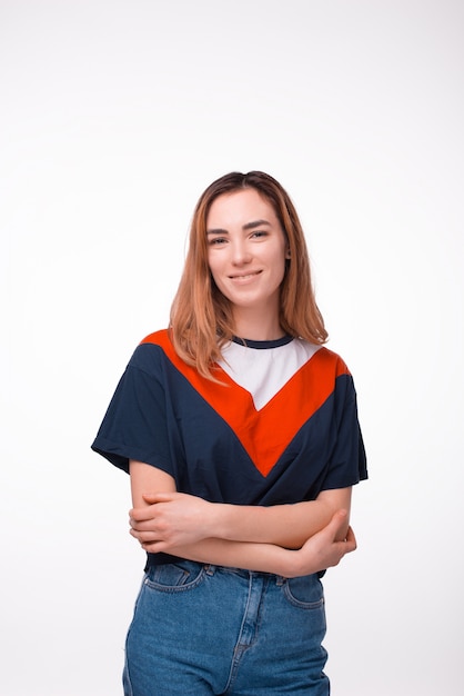 Portrait vertical de joyeuse jeune femme aux bras croisés, debout sur un mur blanc