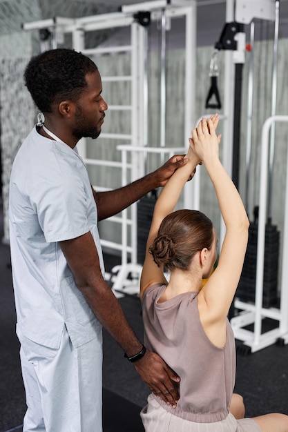 Photo portrait vertical d'un thérapeute afro-américain aidant une jeune femme dans une clinique de réadaptation