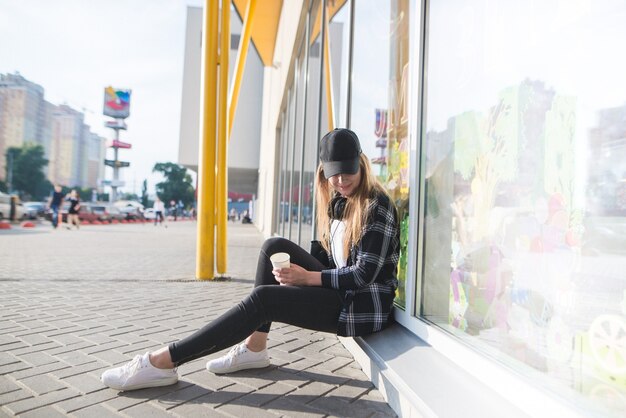 Portrait d'un vêtement décontracté élégant assis à la vitrine avec une tasse de café à la main et regardant vers le bas.