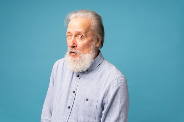 Portrait d'un vieil homme candide barbu blanc clin d'oeil porter des vêtements de bonne apparence isolés sur fond de couleur bleue émotions humaines positives face à des sentiments d'expression