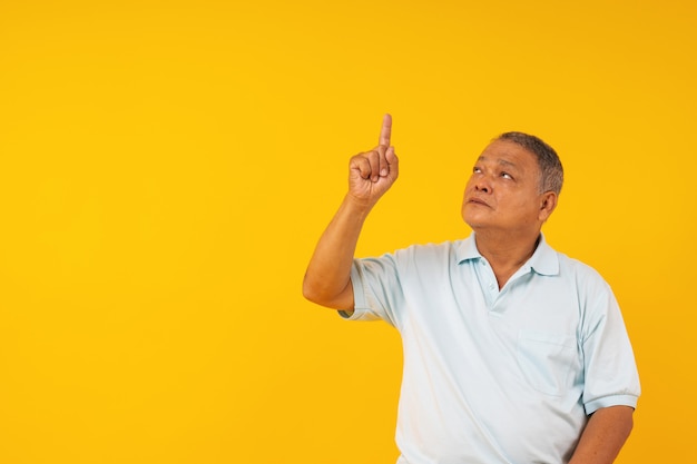 Portrait de vieil homme pointant vers le haut sur le fond jaune, présenter des produits sur le fond et penser actuel
