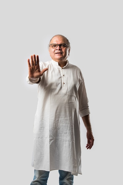 Portrait d'un vieil homme à la retraite indien joyeux porte une kurta blanche, pointant ou présentant ou dans une pose de mains pliées