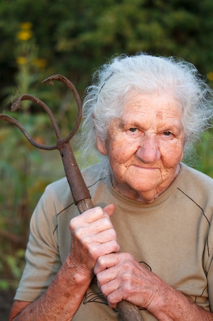 Portrait d'une vieille femme aux cheveux gris tenant une fourche rouillée