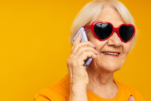 Portrait d'une vieille femme sympathique à lunettes noires parlant au téléphone fond isolé