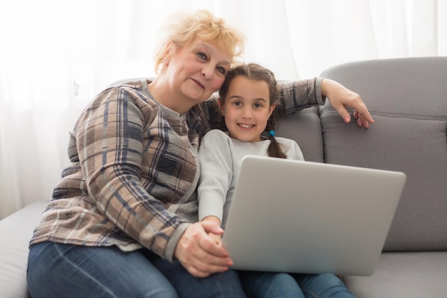 Portrait d'une vieille grand-mère heureuse et d'une petite fille regardant la caméra, grand-mère souriante avec sa petite-fille faisant un appel vidéo, enfants et grand-mère vloggers enregistrant un blog vidéo ou un vlog ensemble