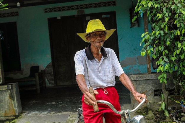 Un portrait d'un vieux fermier indonésien portant un chapeau jaune avec un vieux vélo