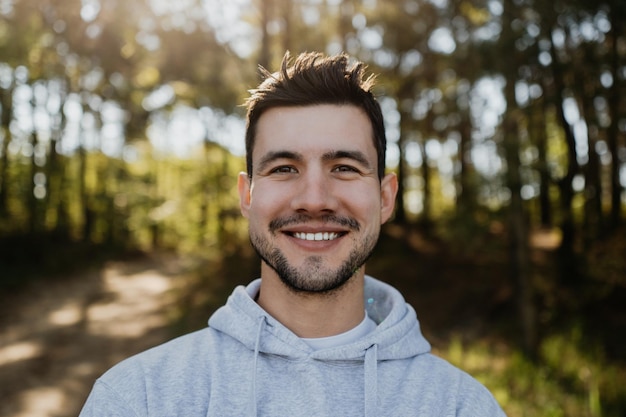 Portrait de visage heureux masculin d'un jeune homme souriant et attrayant posant à l'extérieur en regardant la caméra dans les bois