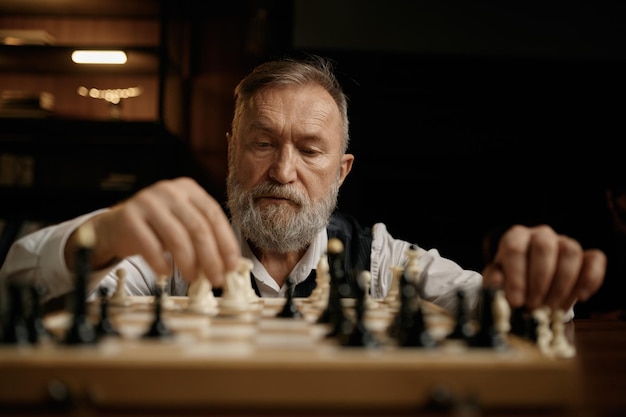 Portrait de visage d'un homme âgé déplaçant une pièce d'échecs à bord pendant un match de compétition