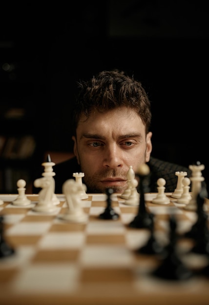 Photo portrait de visage d'un jeune homme réfléchi tenant compte de la position de la pièce d'échecs à bord en planifiant un mouvement stratégique. mise au point sélective et vue rapprochée