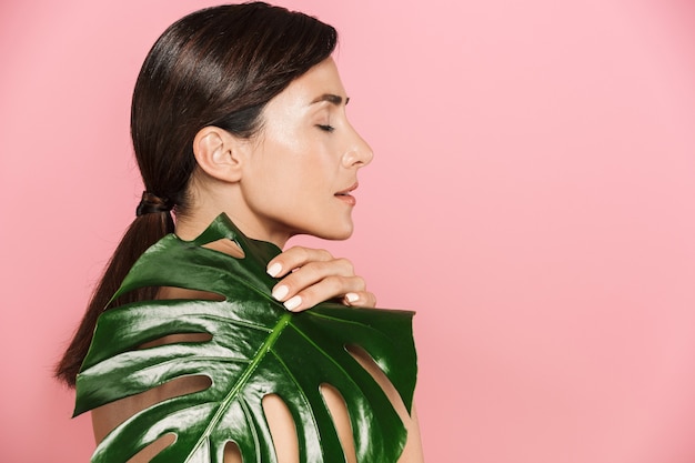 Portrait De Vue De Côté De Beauté D'une Femme Brune Aux Seins Nus Saine Attrayante D'isolement, Couvre Avec La Feuille Tropicale