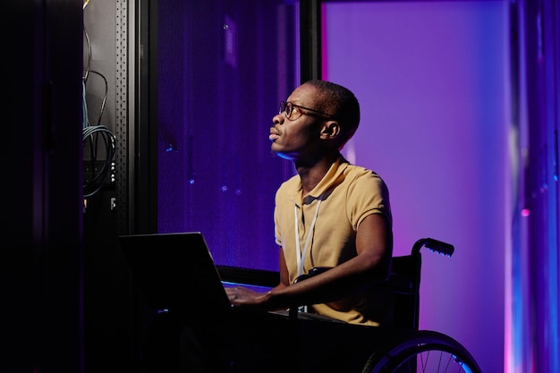 Portrait de vue latérale d'un administrateur système masculin handicapé utilisant un ordinateur lors de la configuration du réseau de serveurs