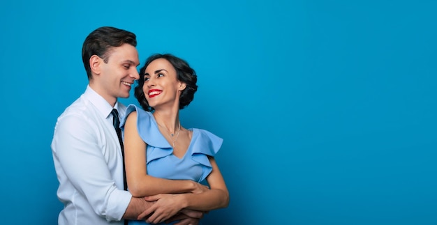 Portrait de vue latérale d'un beau couple charmant et séduisant, charmant et souriant, amoureux, est dans une élégante chemise et une robe isolées sur fond bleu