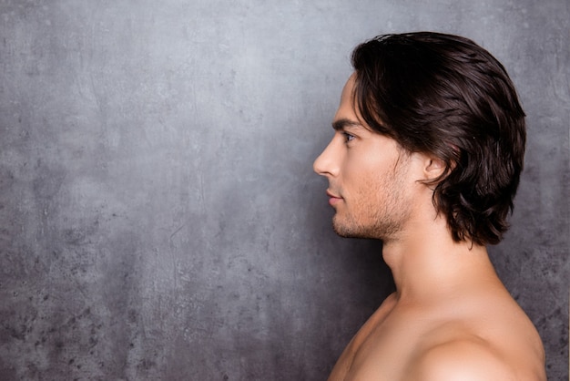 Portrait de vue latérale du jeune homme aux cheveux noirs près du mur gris