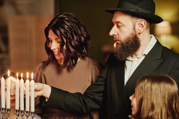 Portrait de vue latérale d'une famille juive orthodoxe allumant une bougie menorah pendant la célébration de hanukkah