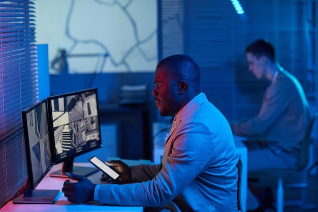 Portrait de vue latérale futuriste d'un homme noir regardant des images de caméras de surveillance dans un centre de sécurité