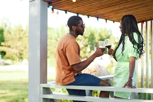 Portrait de vue latérale d'un jeune couple noir bavardant et dégustant un verre de vin sur la terrasse pendant l'outdo