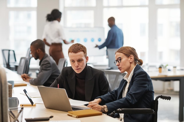 Portrait de vue latérale d'une jeune femme d'affaires utilisant un fauteuil roulant tout en travaillant avec un ordinateur portable au bureau, espace de copie