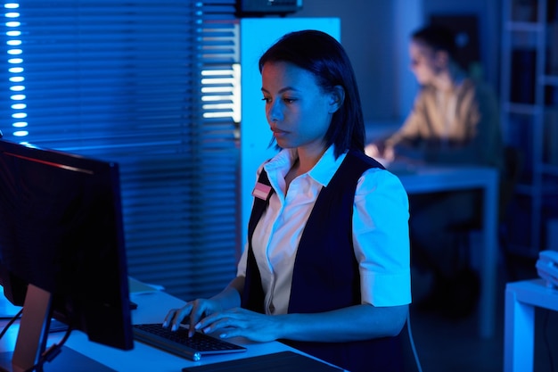 Portrait de vue latérale d'une jeune femme regardant l'alimentation de la caméra de surveillance dans un bureau sombre