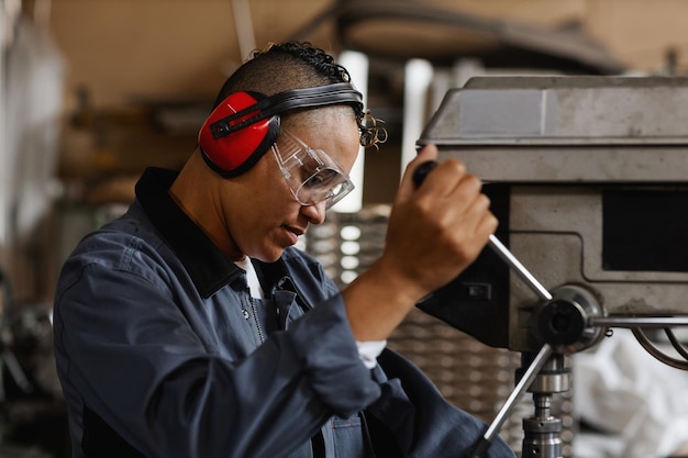 Portrait de vue latérale d'une ouvrière opérant des unités de machine dans un atelier industriel et portant une protection