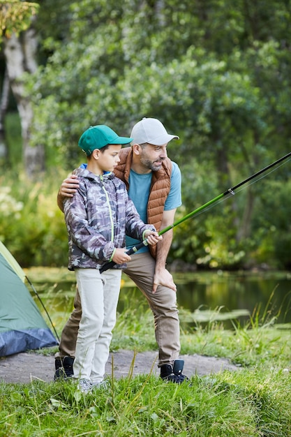 Portrait de vue latérale verticale du père aimant l'enseignement de la pêche à son fils tout en profitant d'un voyage de camping ensemble