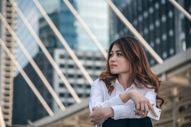 Les portraits de la belle femme asiatique tiennent le smartphone en train de ressentir la tristesse de la dépression en milieu urbain.