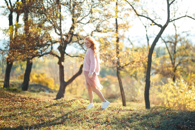 Portraits d'une charmante fille aux cheveux roux avec un joli visage. Fille posant dans le parc automne dans un pull et une jupe de couleur corail. Dans les mains d'une jeune fille une feuille jaune