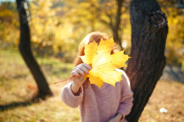 Portraits d'une charmante fille aux cheveux roux avec un joli visage. Fille posant dans le parc automne dans un pull et une jupe de couleur corail. Dans les mains d'une jeune fille une feuille jaune