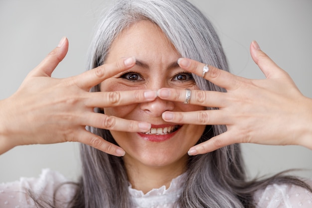 Portraits émotionnels d'une femme mûrie asiatique aux cheveux longs et pâles sur un mur gris