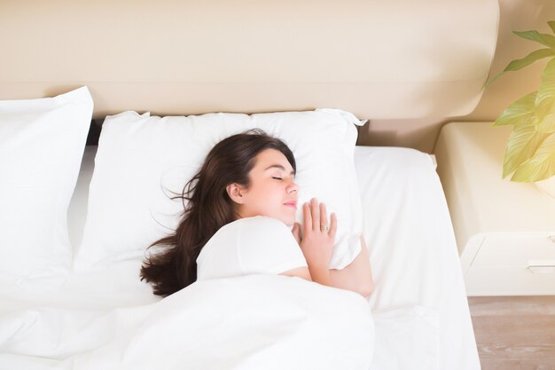 Portreit de jeune femme endormie se trouve dans un lit blanc avec les yeux fermés