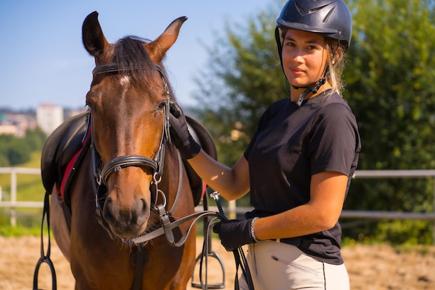 Posant d'une fille blonde caucasienne sur un cheval caressant et choyant un cheval brun, vêtu d'un cavalier noir avec casquette de sécurité