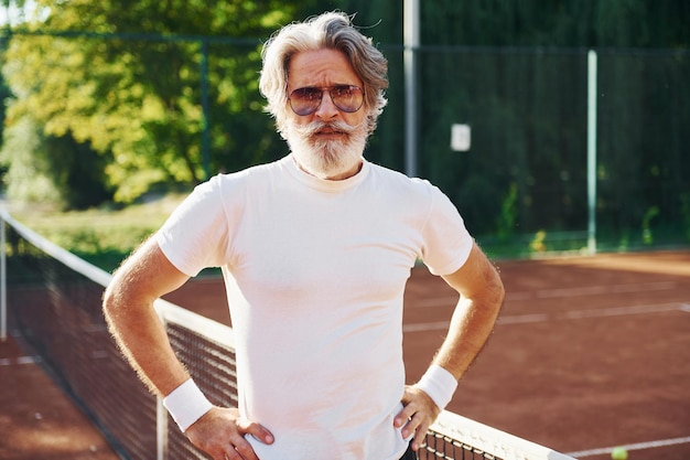 Posant pour un appareil photo dans des lunettes de soleil Senior homme élégant moderne à l'extérieur sur le terrain de sport pendant la journée