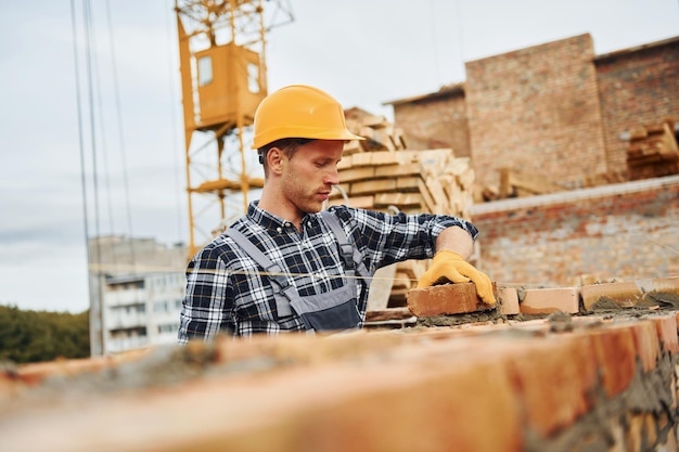 Pose de briques Ouvrier du bâtiment en uniforme et équipement de sécurité a un travail sur la construction