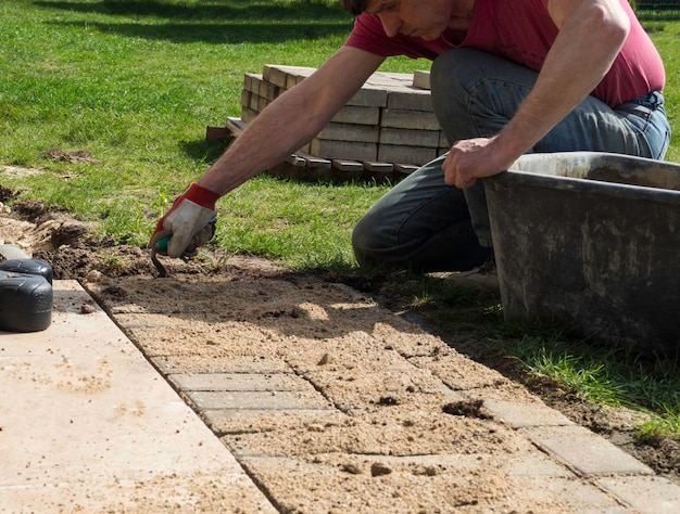 Pose de dalles de pavage en béton gris dans le patio de l'allée de la cour de la maison Ouvrier professionnel