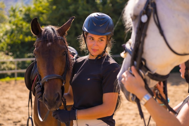 Pose de deux jeunes filles de race blanche cavalières avec leurs chevaux blancs et bruns sur un cheval, vêtus de noir avec des casquettes de sécurité