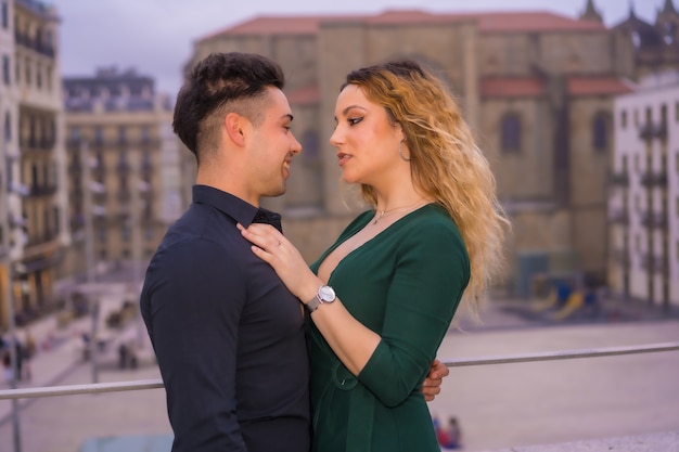 Pose à la mode d'un couple d'amoureux de race blanche dans un costume bleu et une robe verte, se caressant dans la ville