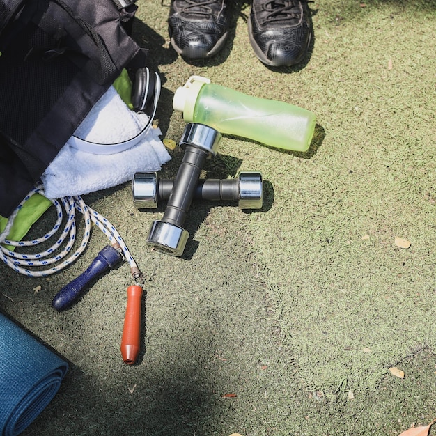 Pose à plat d'équipements de sport sur l'herbe, chaussures, haltères, tapis de yoga, bouteille d'eau et corde à sauter.
