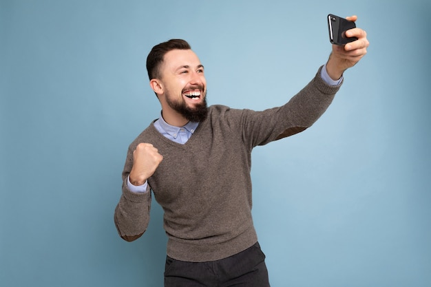 Positif beau jeune homme brunet mal rasé avec barbe portant un pull gris décontracté