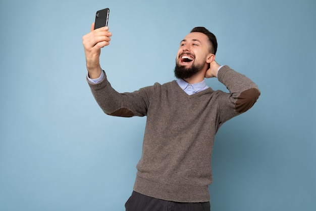 Positif beau jeune homme brunet mal rasé avec barbe portant un pull gris décontracté