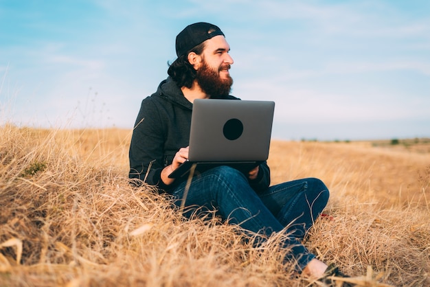 Positif jeune homme barbu travaillant sur l'ordinateur sur un champ