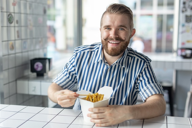 Positif jeune homme élégant, manger des nouilles chinoises dans un café pendant une pause au travail. Le concept de