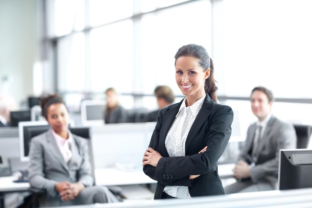 Positif quant à sa carrière dans l'entreprise Jolie jeune femme d'affaires debout avec confiance au bureau avec ses collègues derrière son portrait