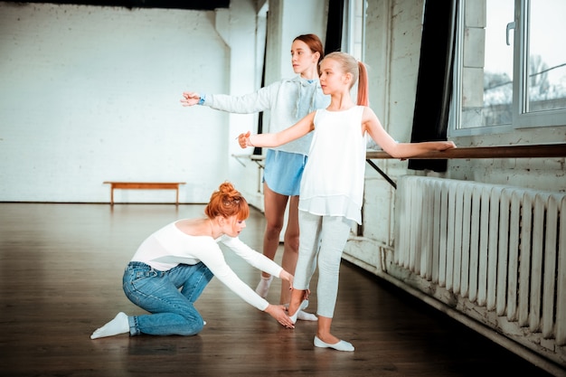 Position des pieds. Professeur de ballet aux cheveux roux portant des pieds de correction de jeans bleu position de son élève