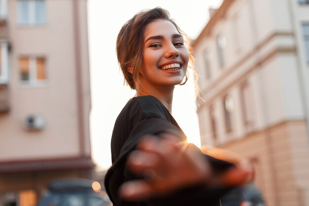 Positive jolie jeune femme avec une coiffure élégante avec un sourire atteignant sa main à la caméra