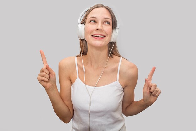 Positive et ludique jeune femme écoutant de la musique avec des écouteurs blancs.