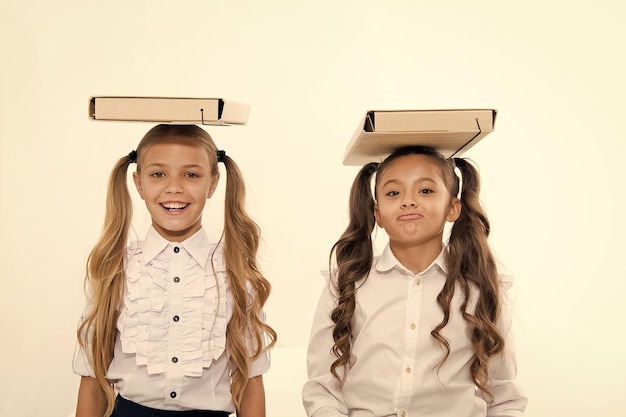 Posture correcte Des écolières avec une jolie coiffure en queue de cheval portent des dossiers sur la tête Des écolières parfaites avec des cheveux fantaisie bien rangés et une posture appropriée portent des dossiers sur la tête Équilibre et fardeau des connaissances