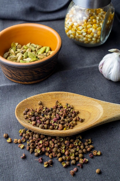 Pot d'argile cardamome papier sichuan dans une cuillère en bois papier piment et baies de genièvre ail et maïs en pot